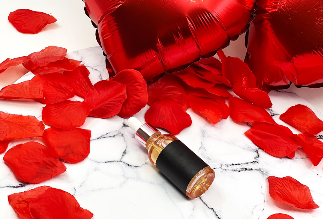 Red heart balloons and rose petals with a bottle.