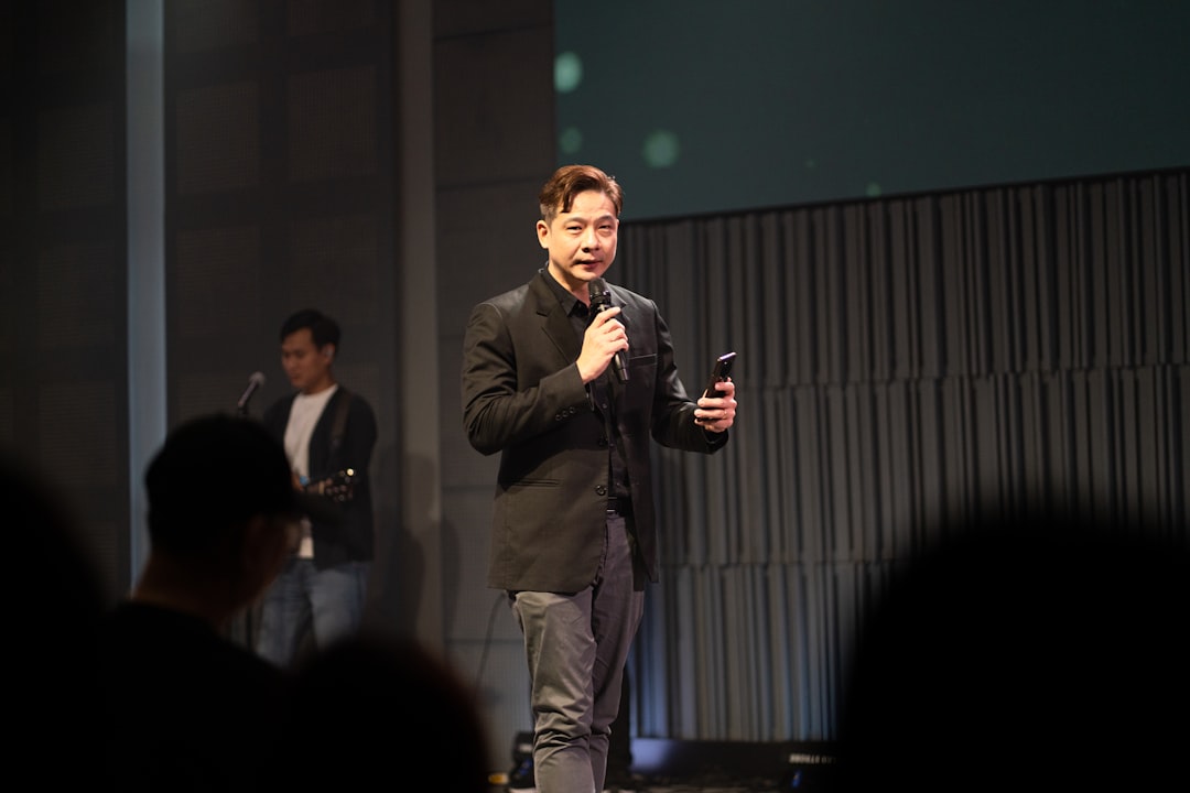 A man in a black jacket speaks into a microphone.