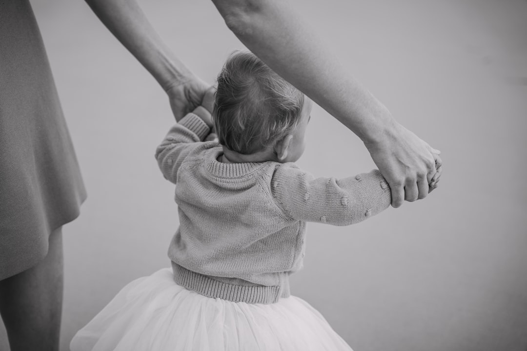 Adults holding a baby's hands, helping her walk.