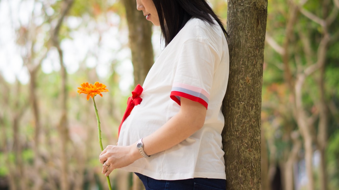 woman holding orange flower leaning on tree