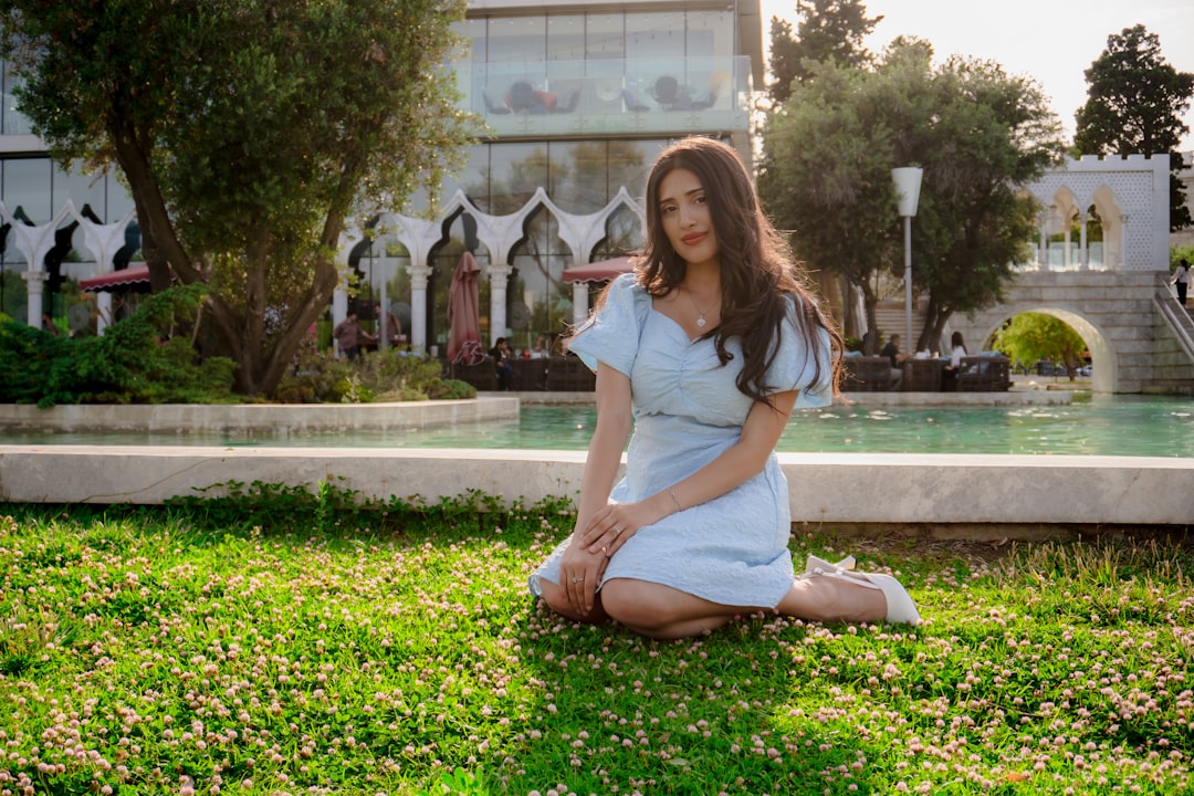 A woman in a light blue dress kneels on grass.