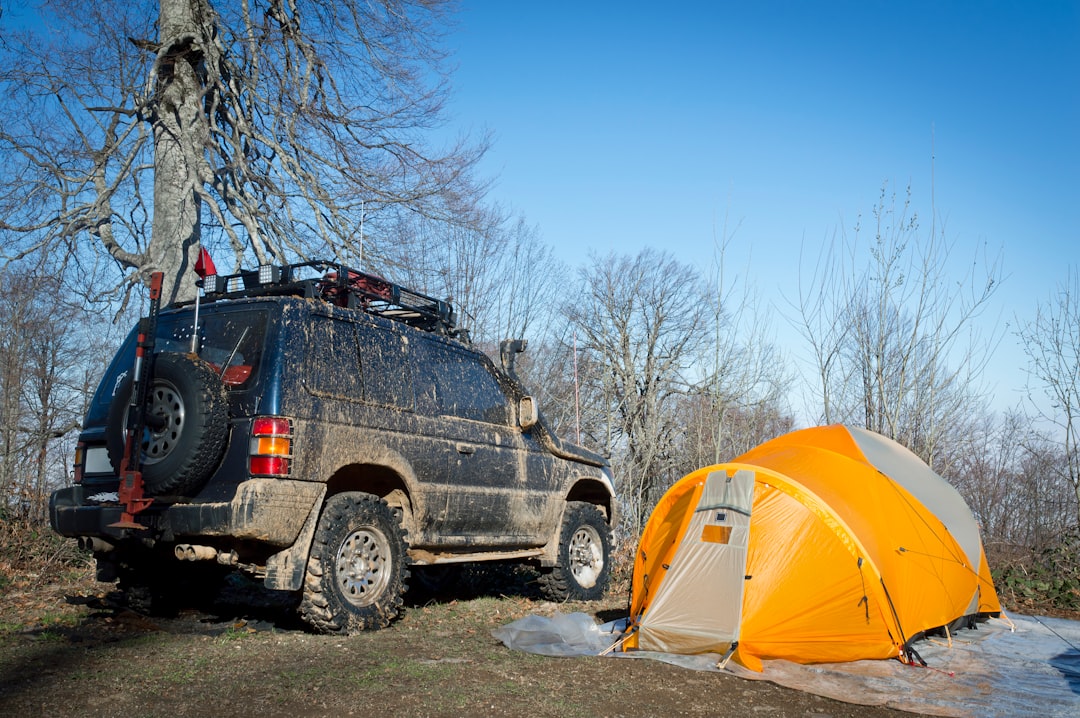 A muddy suv parked next to an orange tent.
