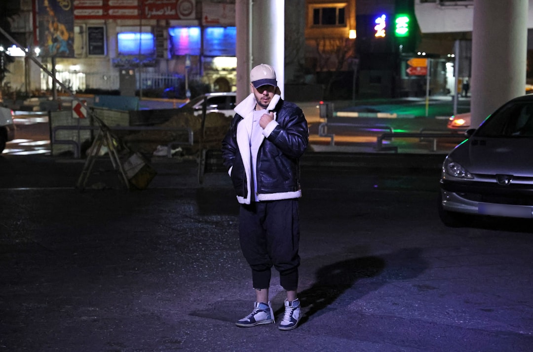 Person in jacket standing on street at night.