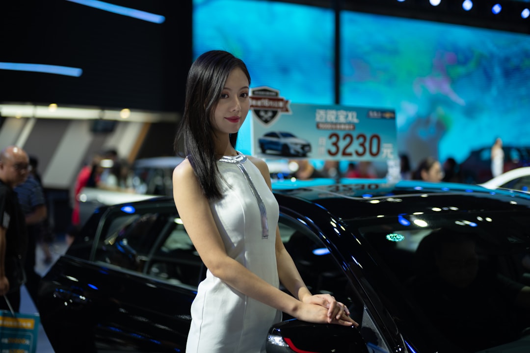A woman in a white dress at a car show.