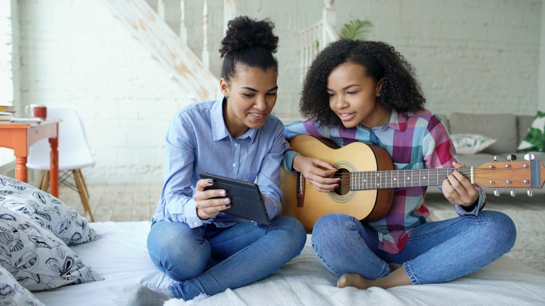 Two young women learning guitar from tablet