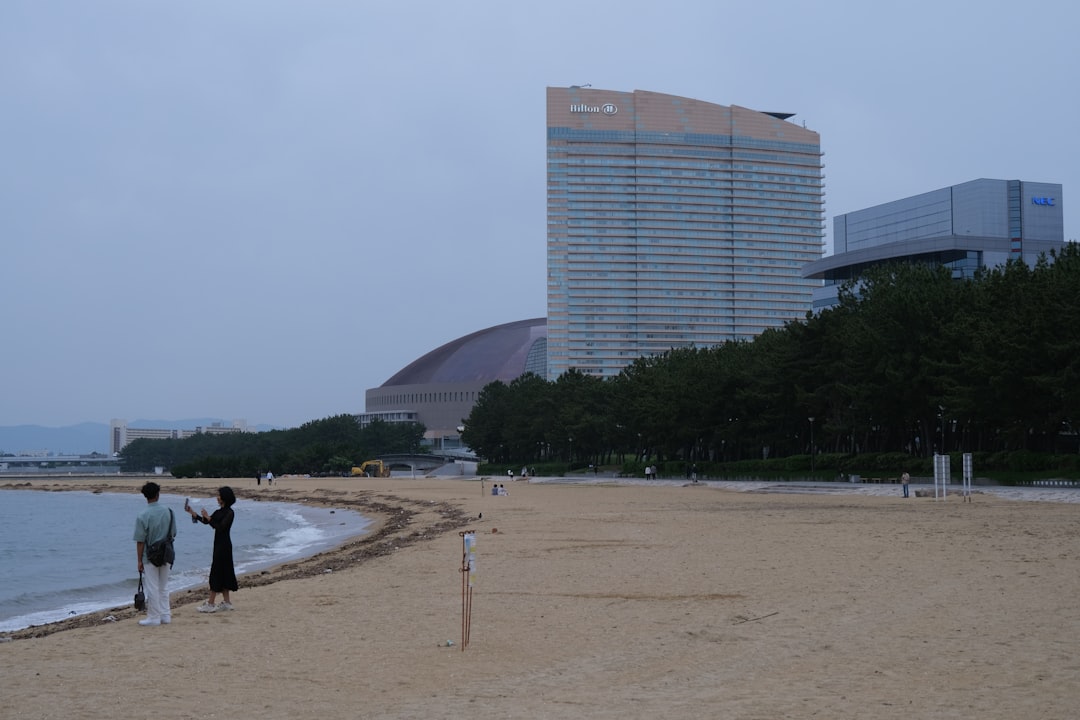 People stand on a beach near tall buildings.