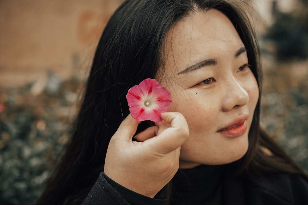 smiling woman wearing crew-neck long-sleeved shirt putting pink flower on her right ear