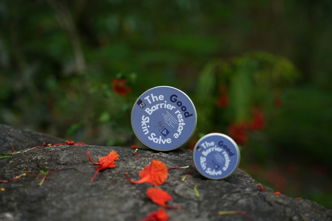 Two tins of skin salve on rocks with flowers.