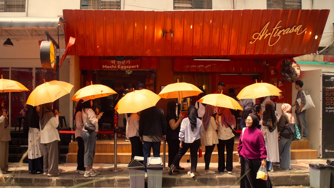People with umbrellas queue outside a shop.