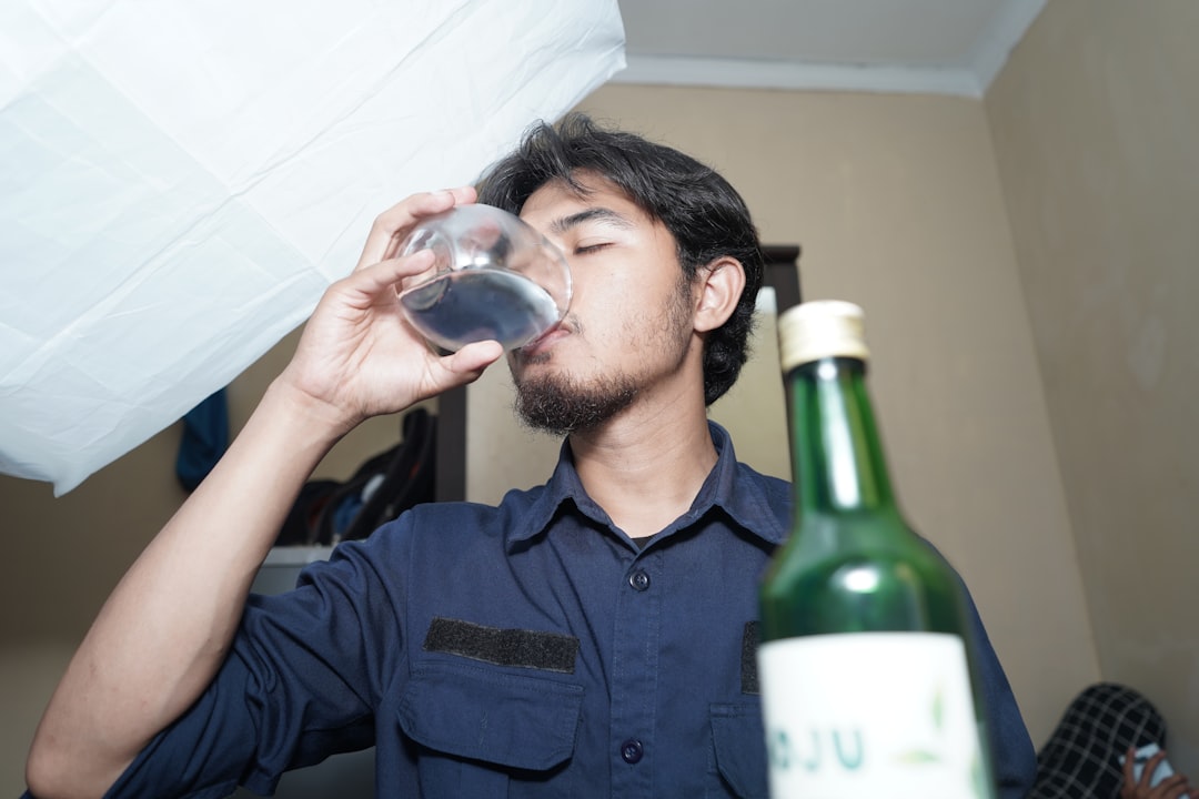 A man drinking from a wine glass next to a bottle
